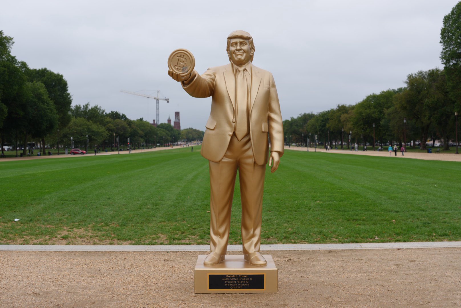 Statua dorata di un uomo in abito che tiene una moneta con simbolo Bitcoin, in un parco alberato